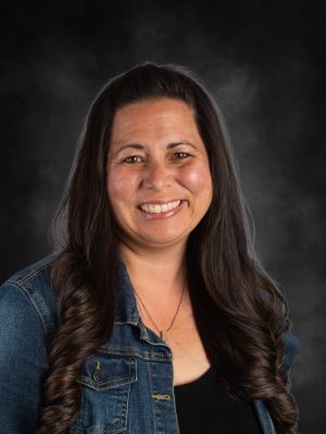 Mrs. Christina Nelson smiling, wearing a denim jacket and a necklace.