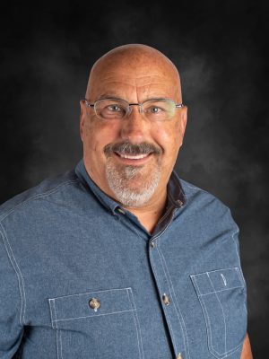 Mr. Mark Bates portrait. Bald man with glasses, goatee, and blue shirt smiling at the camera.